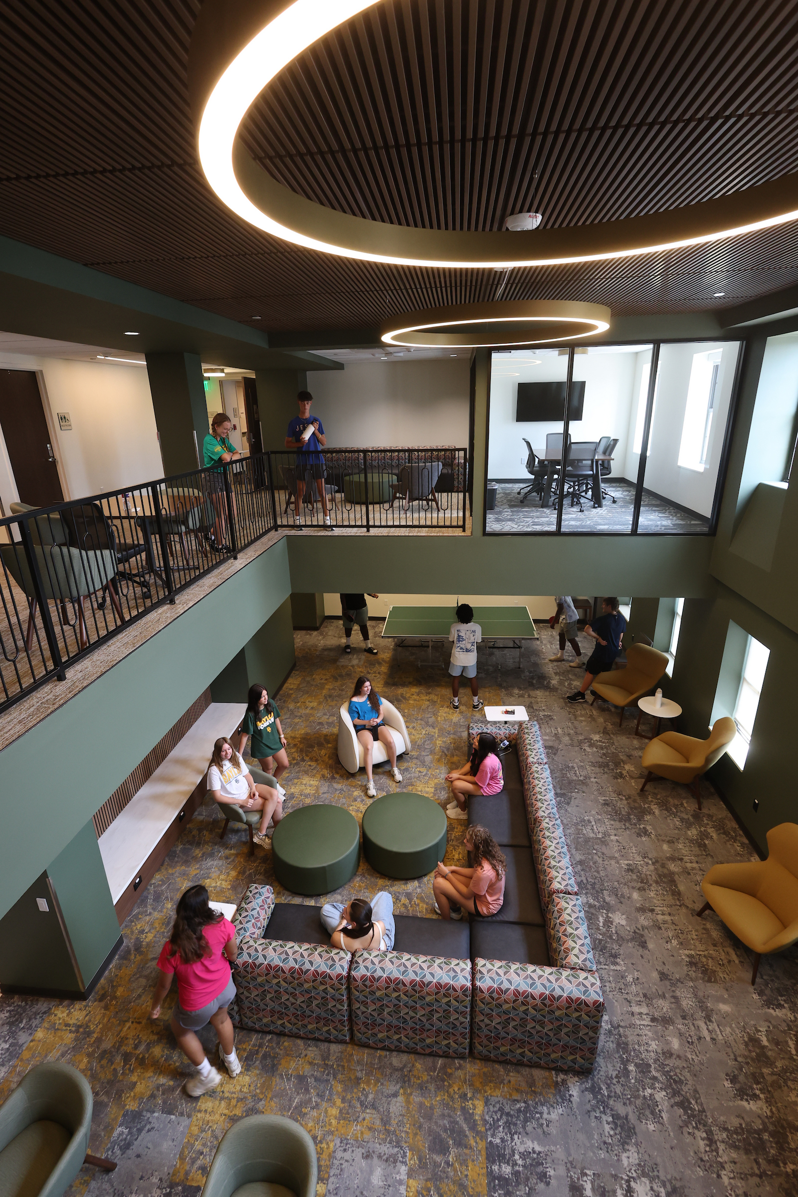 View from the 3rd Floor Commons overlooking the 2nd Floor Commons. Includes seating, lights, and students enjoying the space.