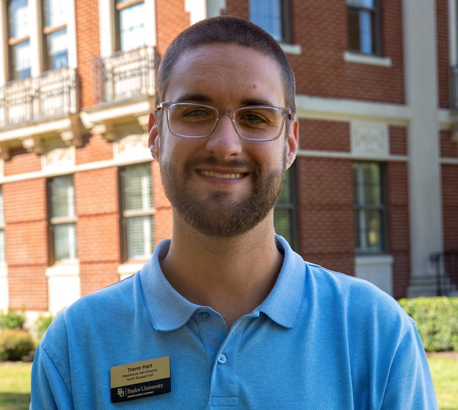 Headshot of LEAD's RHD, Trevor Hart. Male standing in front of Pat Neff Hall wearing blue shirt. Smiling. Wearing glasses.